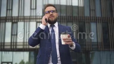 在商业区，成功的<strong>商务人士</strong>打电话，手里拿着一杯咖啡<strong>站在</strong>外面。